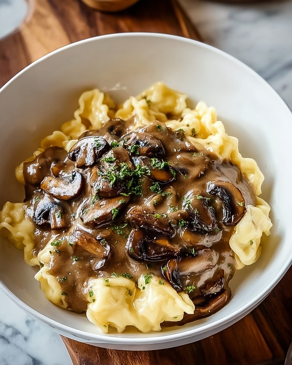 A white bowl holds a creamy pasta dish with two layers: the bottom layer is pale yellow soft pasta with a slightly glossy texture, and the top layer is a thick, brown mushroom sauce with visible sliced mushrooms. The mushrooms are dark brown with a shiny surface, and the sauce has a smooth, rich look. The dish is garnished with small green herb bits sprinkled on top. The bowl sits on a wooden surface with a white marbled texture underneath. photo taken with an iphone --ar 4:5 --v 7