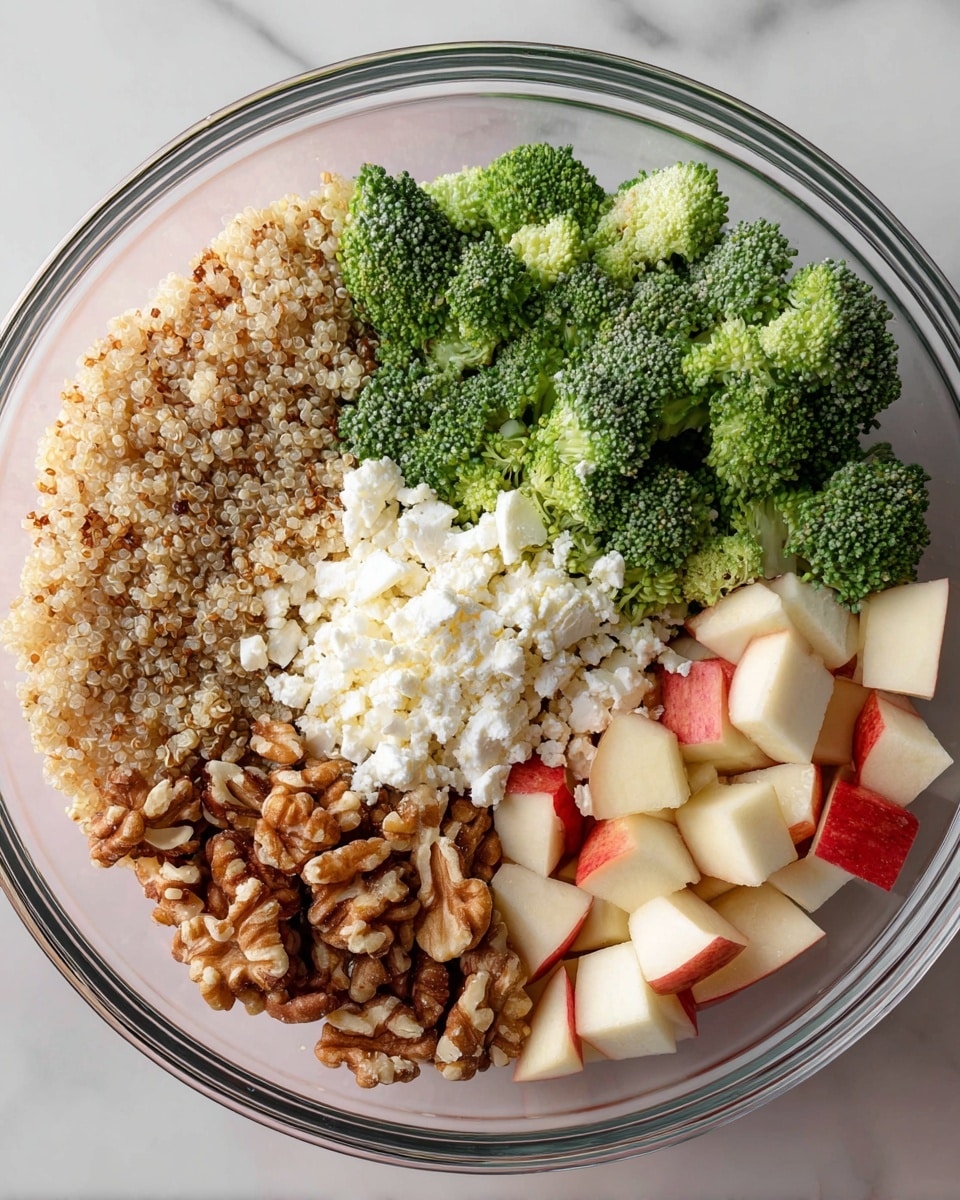 A clear glass bowl holds five distinct layers of ingredients. The top left quarter is filled with small, light brown quinoa grains with a soft texture. Next to it at the top right quarter are bright green, crisp broccoli florets. To the right, a fluffy, white layer of crumbly cheese is placed. Below the quinoa are chopped nuts in mixed brown shades, including darker almonds and lighter walnuts with rough textures. The bottom right quarter has small, neat cubes of apple with red skins and pale flesh. The bowl is set against a white marbled surface. photo taken with an iphone --ar 4:5 --v 7