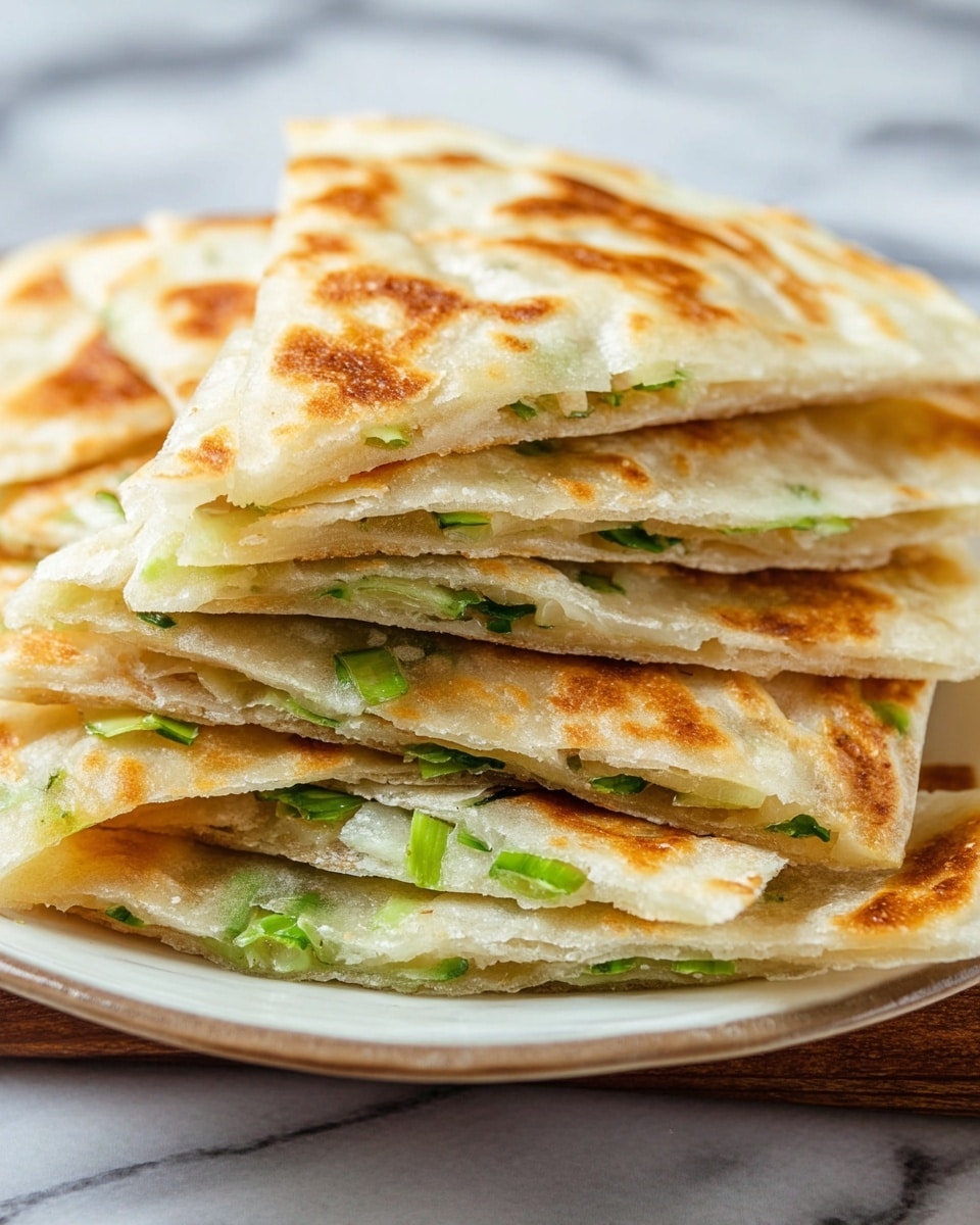 A close-up of a stack of flatbread cut into triangles on a white plate, each piece showing two thin layers of golden-browned dough with a slightly crispy texture, filled with finely chopped green onions visible between the layers, giving a fresh contrast to the warm tones of the flatbread. The stack is arranged casually, showing the layers and filling clearly against a white marbled background. photo taken with an iphone --ar 4:5 --v 7