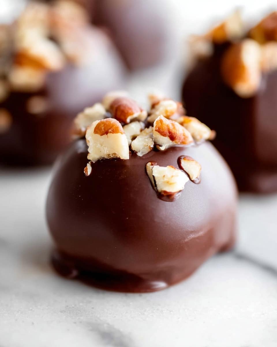 The image shows round chocolate-covered balls placed on a white marbled surface. Each ball is coated in smooth, shiny dark brown chocolate and topped with pieces of pecans that add textures with their light brown and cream colors. The focus is on the front ball, showing details of the glossy chocolate and nut pieces, while more balls are softly blurred in the background. photo taken with an iphone --ar 4:5 --v 7