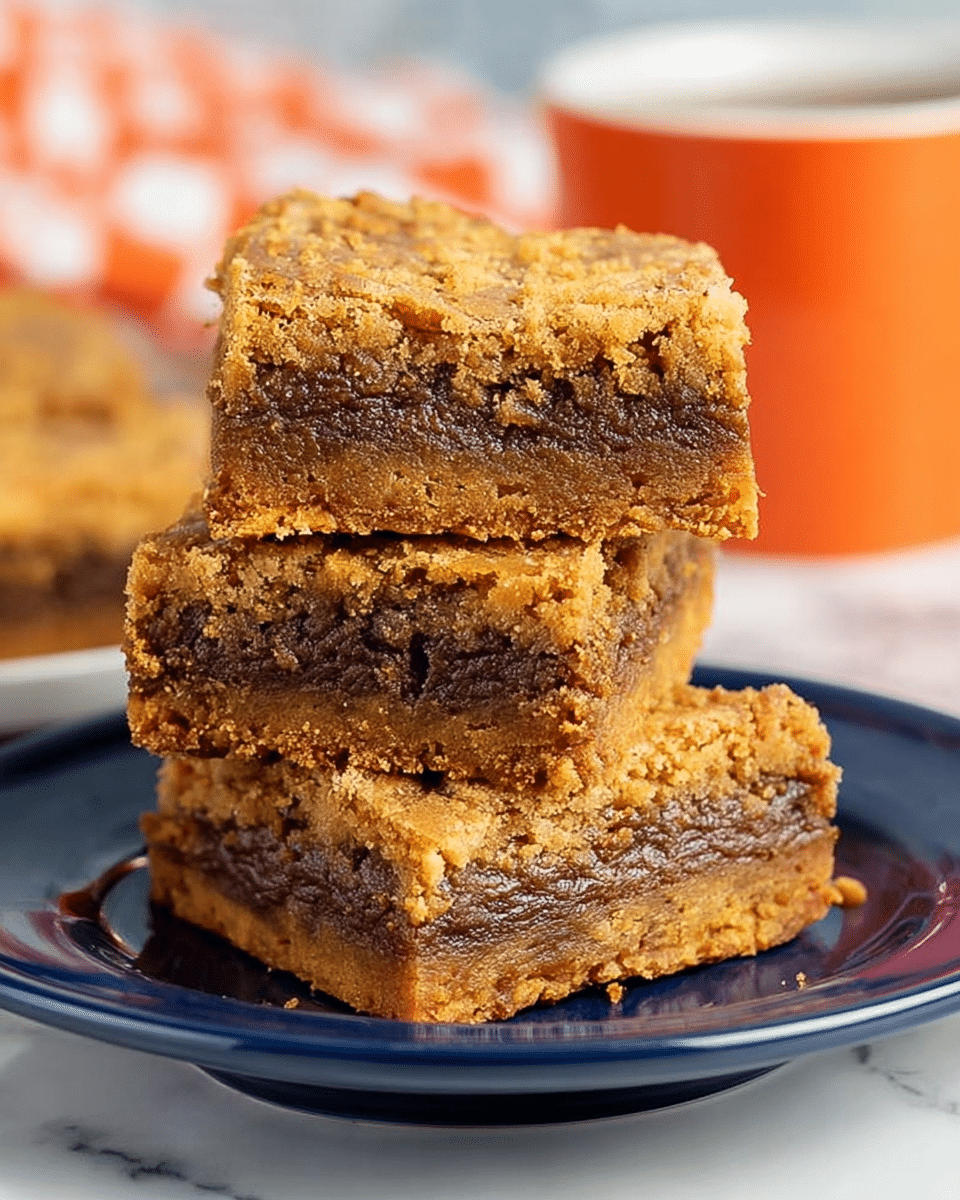 Three thick bar cookies are stacked on a shiny dark blue plate placed on a white plate. Each bar has two layers, a crumbly golden brown crust on top and bottom with a soft, gooey darker brown filling in the middle. The bars have a rough, slightly cracked texture on top. The background is a white marbled surface with an orange cup blurred out behind the plate. photo taken with an iphone --ar 4:5 --v 7
