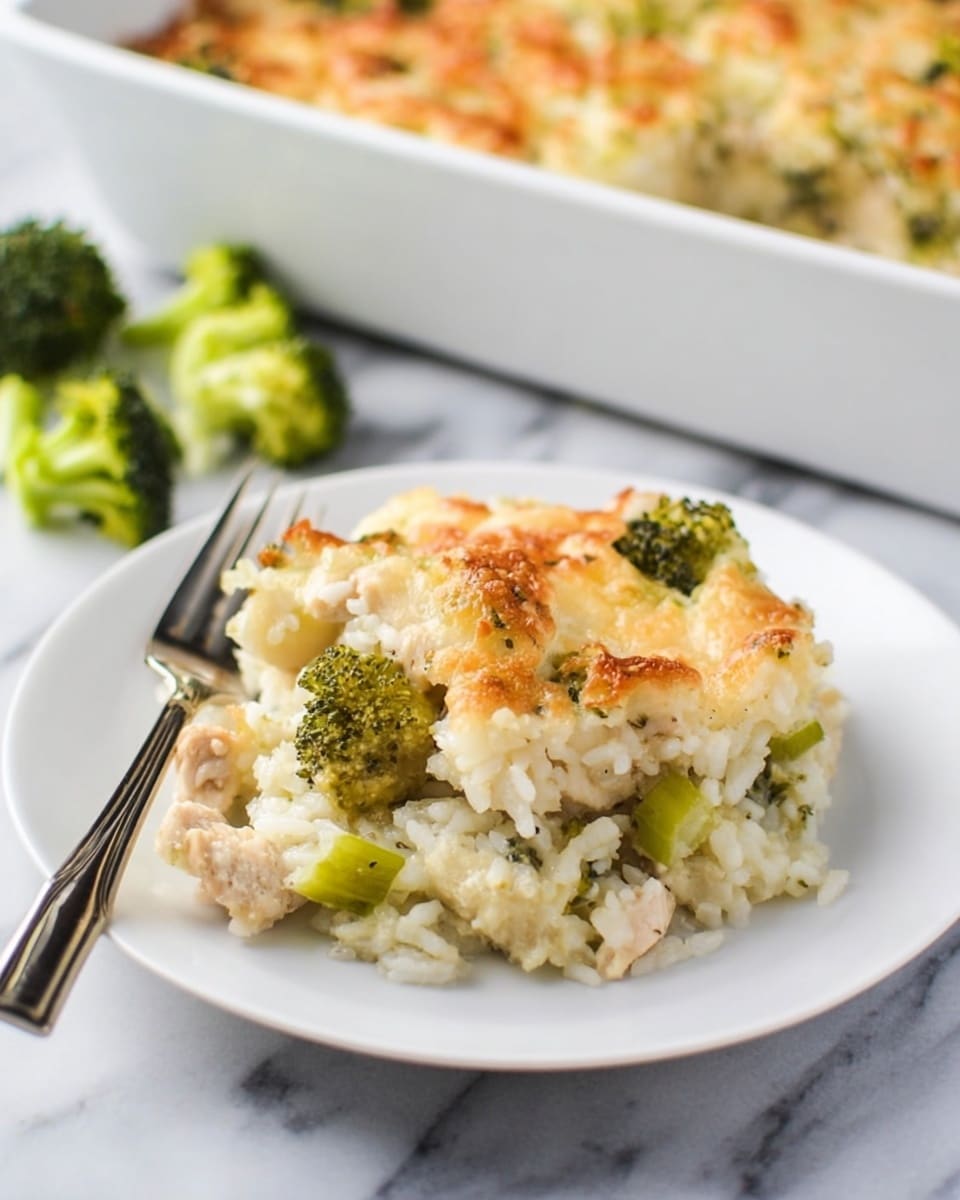 A white plate holds a serving of baked casserole with three visible layers: a base of light-colored rice mixed with small pieces of green broccoli, a middle layer of tender light beige chicken chunks, and a top layer of melted golden-brown cheese with some crispy spots. The dish appears soft with a slightly browned, bubbly texture on top. A silver fork rests on the left side of the plate. In the background, part of a white baking dish filled with the same casserole is slightly blurred, sitting on a white marbled surface with a few broccoli florets nearby. Photo taken with an iphone --ar 4:5 --v 7
