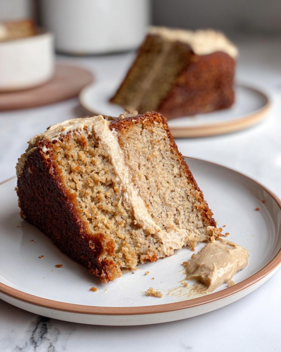 The image shows two thick slices of dense, moist cake on a white plate with a thin tan rim, placed on a white marbled surface. Each slice has one brown, slightly caramelized crust layer on the outside and a soft, crumbly beige middle layer that looks textured with small bits inside. The front slice has some creamy light brown frosting spread unevenly on one side, with a small smear of frosting on the plate next to it. In the blurry background, there is another slice on a similar white plate with the same tan rim. The lighting is soft and natural, emphasizing the cake’s texture and color contrast. photo taken with an iphone --ar 4:5 --v 7