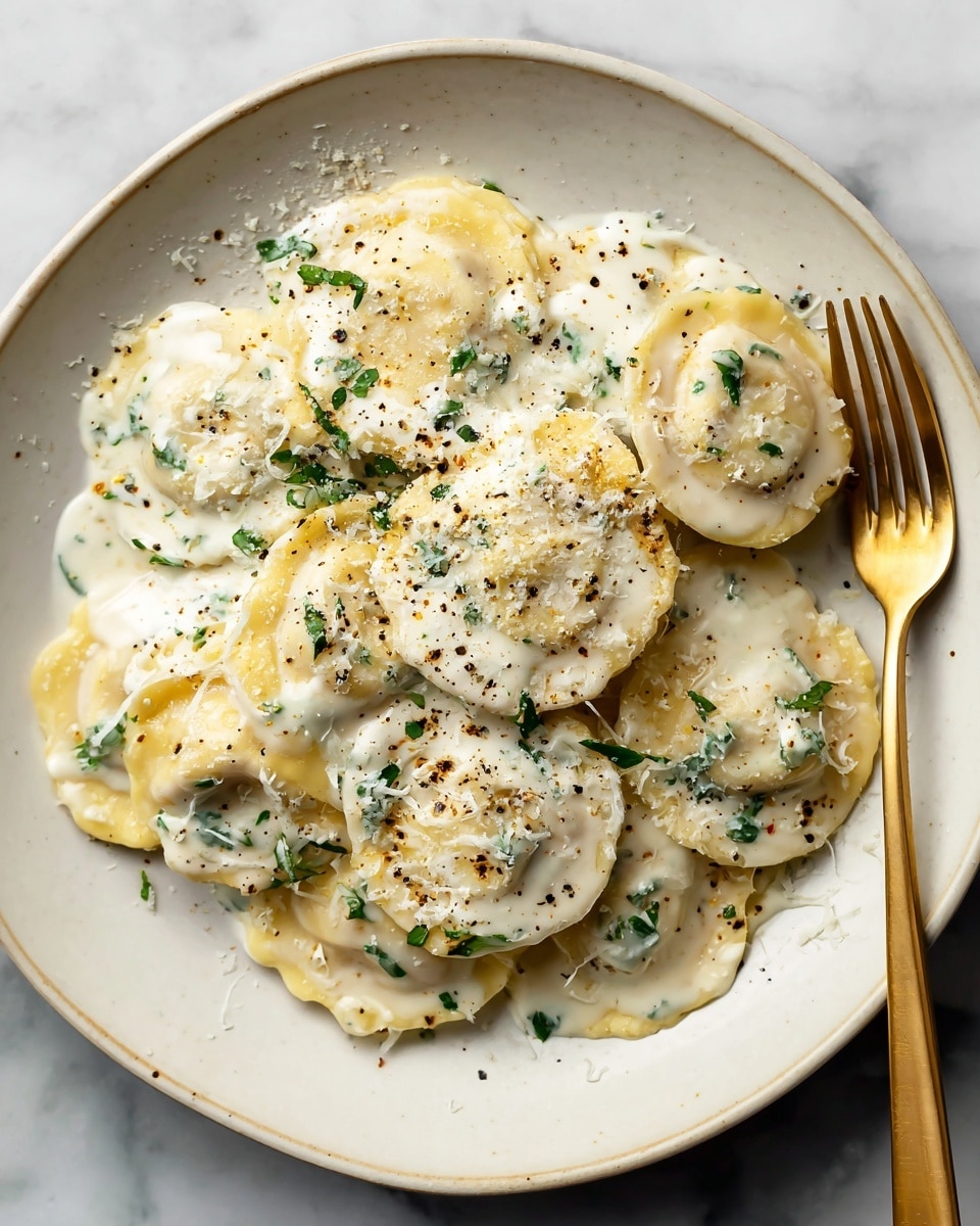 A white plate holds a pile of round ravioli with slightly crinkled edges, each piece pale yellow and covered in a creamy white sauce flecked with small green herbs. The ravioli are layered loosely in a single stack, topped with a light dusting of grated cheese and a sprinkle of black pepper. A golden fork rests on the right edge of the plate, all set on a white marbled surface. photo taken with an iphone --ar 4:5 --v 7