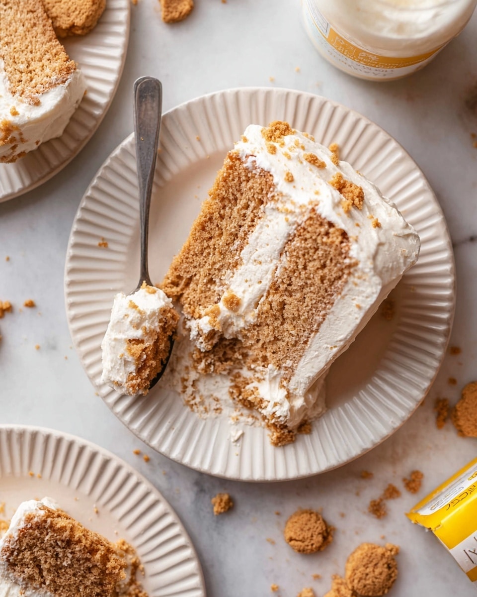 A white ridged plate holds a slice of three-layered cake with light brown, crumbly sponge. Between each layer, and on the sides, there is a thick spread of smooth, white frosting. A spoon rests on the plate with a bite-sized piece of cake covered with frosting. Around the plate and on the white marbled surface, there are cookie crumbs and broken cookie pieces in golden brown color. Another white ridged plate with two smaller cake slices is partially visible at the bottom left. Photo taken with an iphone --ar 4:5 --v 7