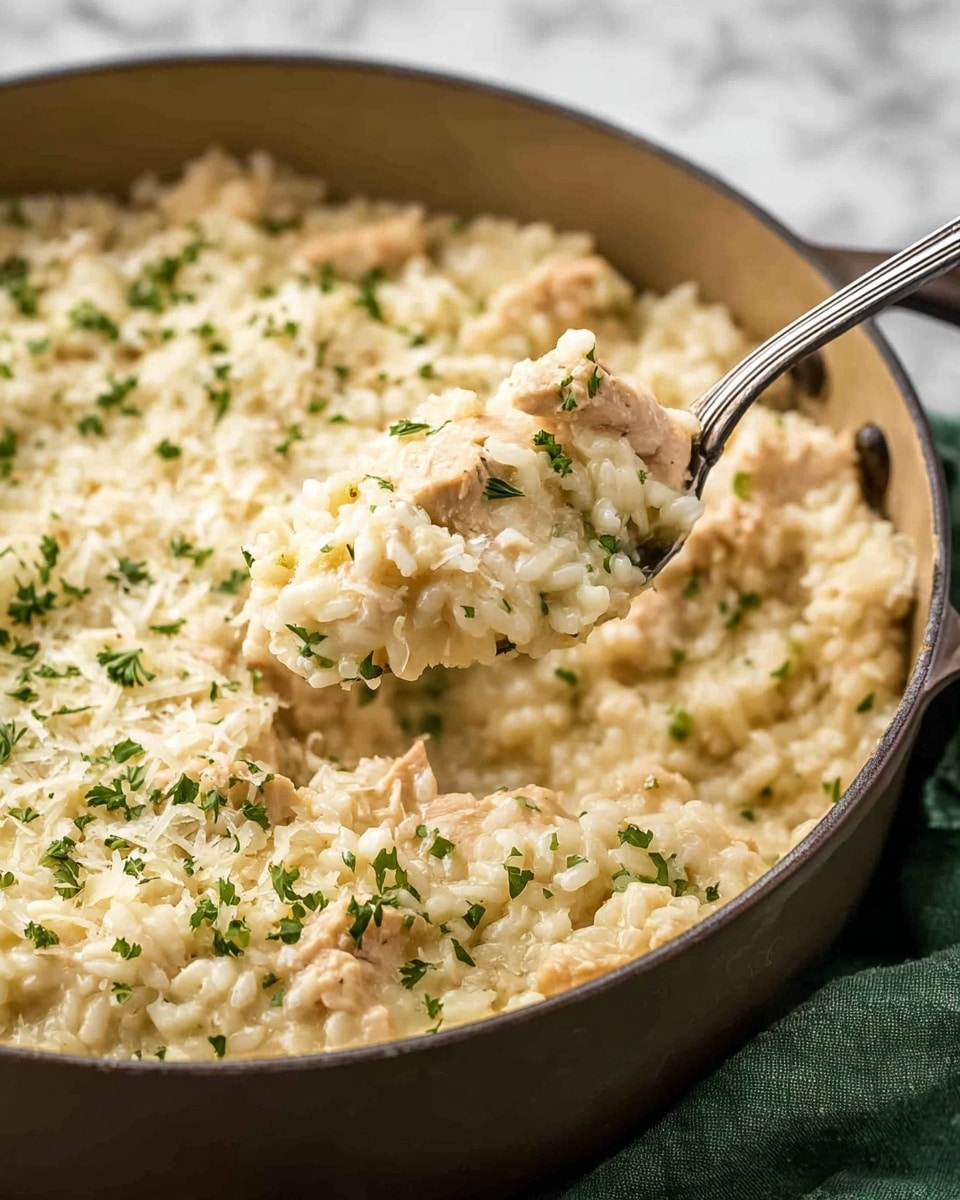 A close-up of creamy risotto with small chunks of chicken mixed in, all inside a light brown cooking pot. The risotto looks soft and slightly thick, with a light beige color dotted with green parsley flakes on top. A silver fork lifts a spoonful of the risotto, showing the texture of tender rice grains and tender chicken pieces covered in the creamy sauce. The background surface is a white marbled texture with a folded green cloth partially visible on the right side. photo taken with an iphone --ar 4:5 --v 7