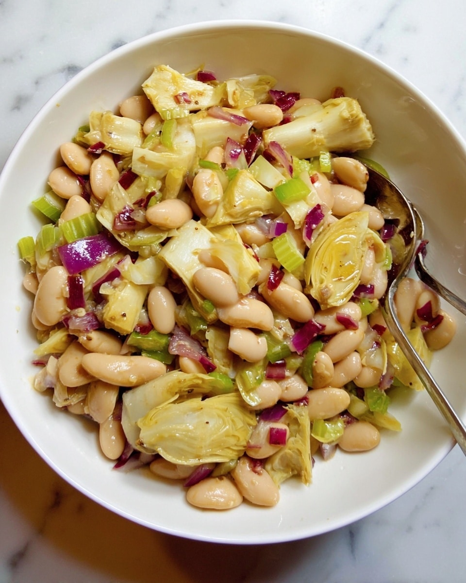 A white bowl filled with a mixed salad showing three main layers: the bottom layer has light tan beans, the middle layer shows pale yellow artichoke pieces with varied shapes, and the top layer contains bits of finely chopped purple-red onion and some green celery slices. The textures appear soft and moist, and a metal spoon is placed inside the bowl. The image background is a white marbled surface. Photo taken with an iphone --ar 4:5 --v 7