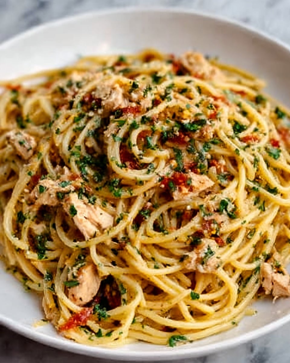 A white shallow bowl filled with spaghetti pasta mixed with small pieces of cooked chicken, red bell peppers, and finely chopped green herbs, all evenly spread throughout the dish. The spaghetti noodles are lightly coated in a sauce, giving them a slightly shiny, golden color. The chicken pieces are tender and white, scattered on top and through the pasta, while the red bell peppers add bright red bits of color. Green herbs sprinkle the surface, adding a fresh, textured look. The dish sits on a white marbled surface. Photo taken with an iphone --ar 4:5 --v 7