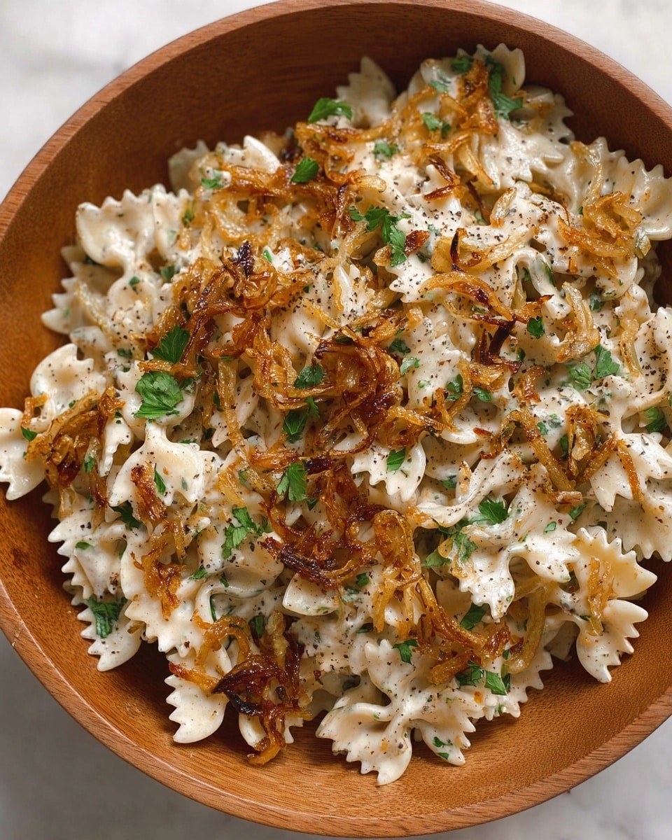This dish shows a single layer of bowtie pasta coated evenly with a creamy white sauce speckled with green herbs and black pepper. On top, there are scattered golden-brown fried onion pieces adding texture and color contrast. Fresh green cilantro leaves are placed intermittently over the pasta, adding a touch of brightness. The food is served in a round wooden bowl with smooth edges, placed on a white marbled surface. photo taken with an iphone --ar 4:5 --v 7