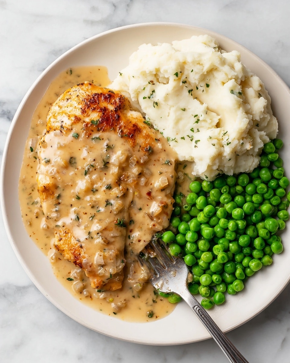 A white plate holds a meal with three parts: on the left, a grilled chicken breast with a light brown creamy sauce that has small chopped onions and green herbs, topped with black pepper. In the middle, there is a fluffy mound of white mashed potatoes, also covered in the same light brown sauce, with bits of onion and herbs. On the right, a pile of bright green peas adds a fresh pop of color. A silver fork rests at the edge of the plate on a white marbled surface. Photo taken with an iphone --ar 4:5 --v 7