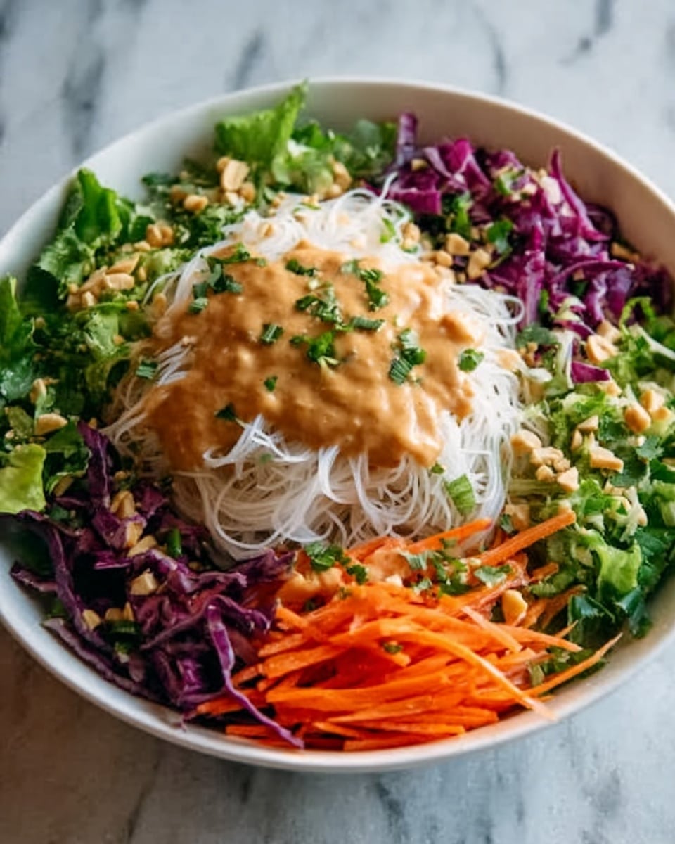 A white bowl filled with a colorful salad sits on a white marbled surface. The salad has thin white rice noodles in the center, topped with a creamy brown dressing. Surrounding the noodles are shredded purple cabbage on the left, green leafy lettuce on the bottom left, and thin orange carrot strips on the top right. Small pieces of chopped nuts and fresh green herbs are scattered over the dressing and noodles. The textures show a mix of soft noodles, crunchy vegetables, and creamy sauce creating a fresh, layered look. Photo taken with an iphone --ar 4:5 --v 7