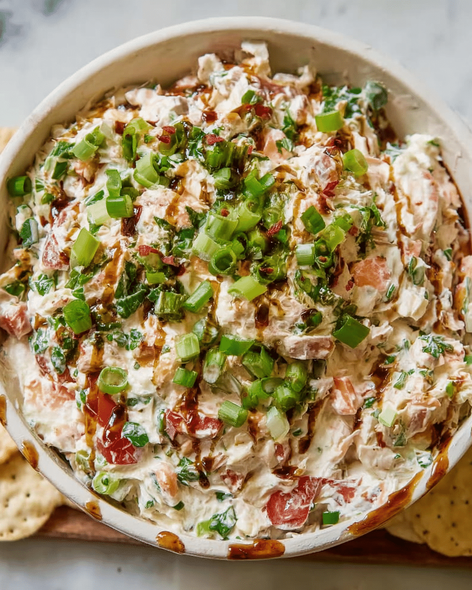 A close-up view of a chunky salad mix placed in a wooden bowl, showing at least three layers: the bottom layer with creamy white base mixed with finely chopped green herbs and bits of red vegetables; the middle layer has more visible chunks of diced tomato and green onion pieces scattered evenly; and the top layer is sprinkled with chopped green onions and hazelnuts, with a drizzle of dark brown sauce adding contrast. The bowl is surrounded by pale, lightly salted tortilla chips on a white marbled surface. Photo taken with an iphone --ar 4:5 --v 7