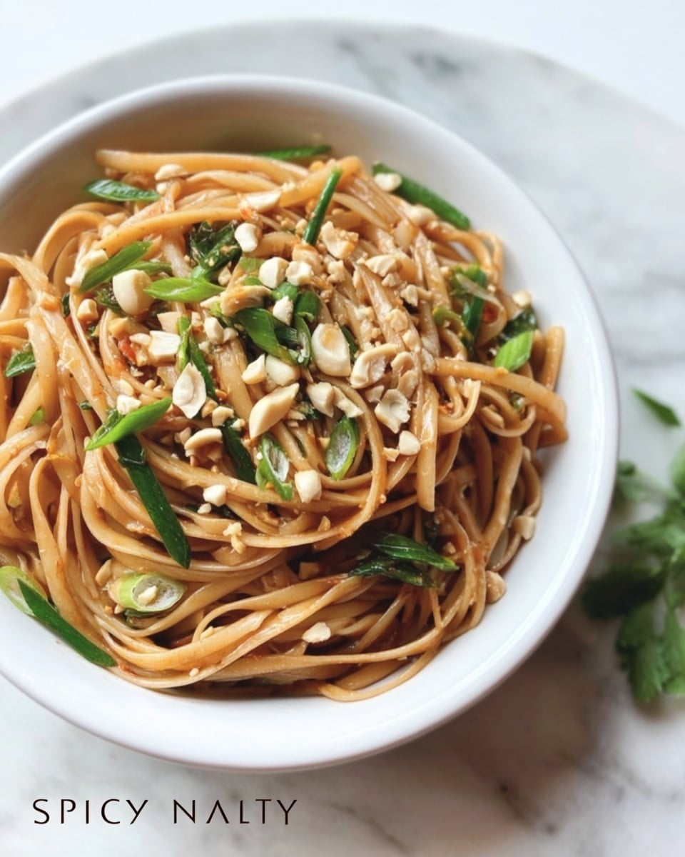 The image shows a white oval bowl filled with spicy Thai noodles. The noodles are light brown, soft, and twisted, mixed with small pieces of green onions and crushed peanuts. The bowl sits on a white marbled surface, with some green parsley leaves in the background. The dish looks fresh and vibrant, with a mix of textures from the smooth noodles and crunchy peanuts. photo taken with an iphone --ar 4:5 --v 7