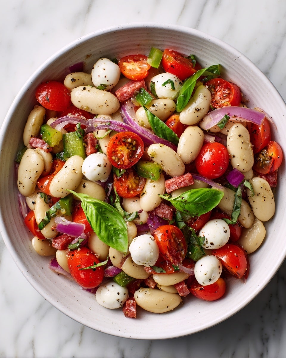 A white bowl filled with a colorful bean salad layered with large white butter beans forming the base, bright red halved cherry tomatoes scattered evenly on top, small white mozzarella balls mixed throughout, and chopped green bell peppers adding a fresh crunch. Bits of purple onion are visible in small pieces, and thin slices of reddish-brown salami pieces are spread over the salad. The mix is garnished with finely chopped green herbs and a sprinkle of black pepper. The bowl sits on a white marbled surface. photo taken with an iphone --ar 4:5 --v 7
