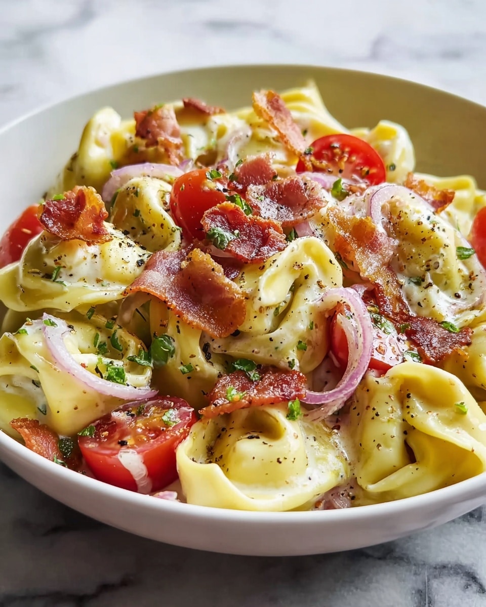 A white bowl filled with creamy tortellini pasta, showing about two layers of round pasta filled with cheese, coated in a rich white sauce. Scattered on top are halved bright red cherry tomatoes, thin slices of red onion, and crisp pieces of browned bacon. The dish is sprinkled with fresh green herbs and cracked black pepper, giving it a colorful and textured look. The bowl sits on a cloth against a white marbled surface, creating a fresh, inviting scene. photo taken with an iphone --ar 4:5 --v 7