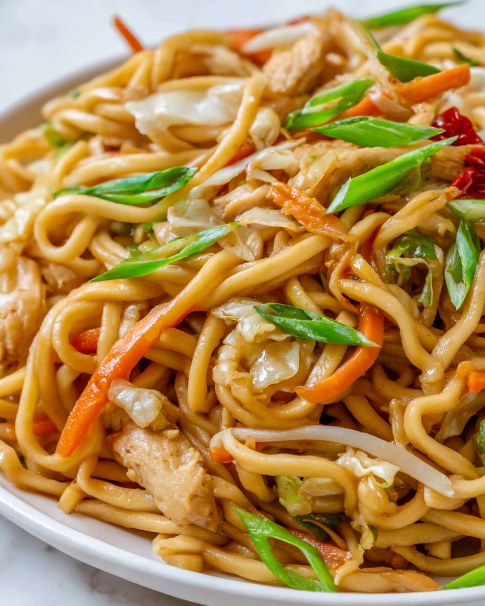 A close-up view of a white plate filled with stir-fried thick noodles, showing multiple layers of light brown noodles mixed with small pieces of cooked chicken, thin slices of white and orange cabbage, and bright orange carrot shreds. Scattered throughout the noodles are fresh green onion slices, small pieces of bean sprouts, and bits of red chili pepper, adding spots of green, white, and red colors. The textures range from smooth, slightly shiny noodles to the crispness of the vegetables and the tender chicken pieces, all arranged loosely and naturally on the plate with a white marbled background. Photo taken with an iphone --ar 4:5 --v 7