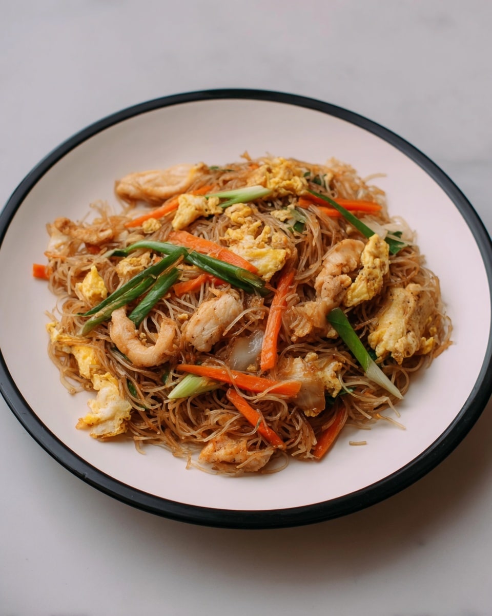 A white plate with a black rim holds a serving of stir-fried noodles mixed with several ingredients, sitting on a white marbled surface. The base layer consists of thin, brownish stir-fried noodles with a slightly glossy texture. Scattered throughout are pieces of lightly browned chicken strips, placed both on top and throughout the noodle bed. Bright orange carrot sticks and thin green onion strips are mixed well in the noodles, adding pops of color. Small chunks of scrambled egg, golden and slightly crispy on the edges, are also visible above the noodles. The dish looks well-cooked and mixed, showing a combination of soft, tender, and slightly crispy textures. photo taken with an iphone --ar 4:5 --v 7