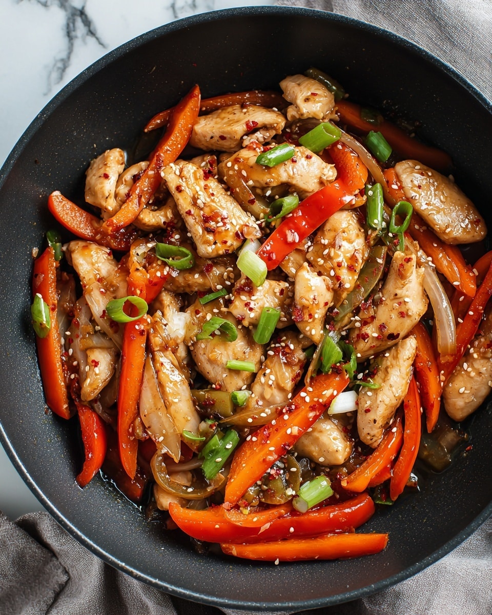 The image shows a black pan filled with a stir-fry dish consisting of three main layers. The bottom layer includes cooked onion pieces that are light brown and translucent with a soft texture. The middle layer has bright red bell pepper strips, slightly shiny from the sauce, scattered evenly across the dish. The top layer consists of chunks of cooked chicken that are light golden brown with a glossy finish, mixed with pieces of green onion that add fresh green color. The stir-fry is sprinkled with small white sesame seeds and red chili flakes, adding extra texture and color. The pan is placed on a surface with a white marbled texture, and a gray cloth is visible to the left. photo taken with an iphone --ar 4:5 --v 7
