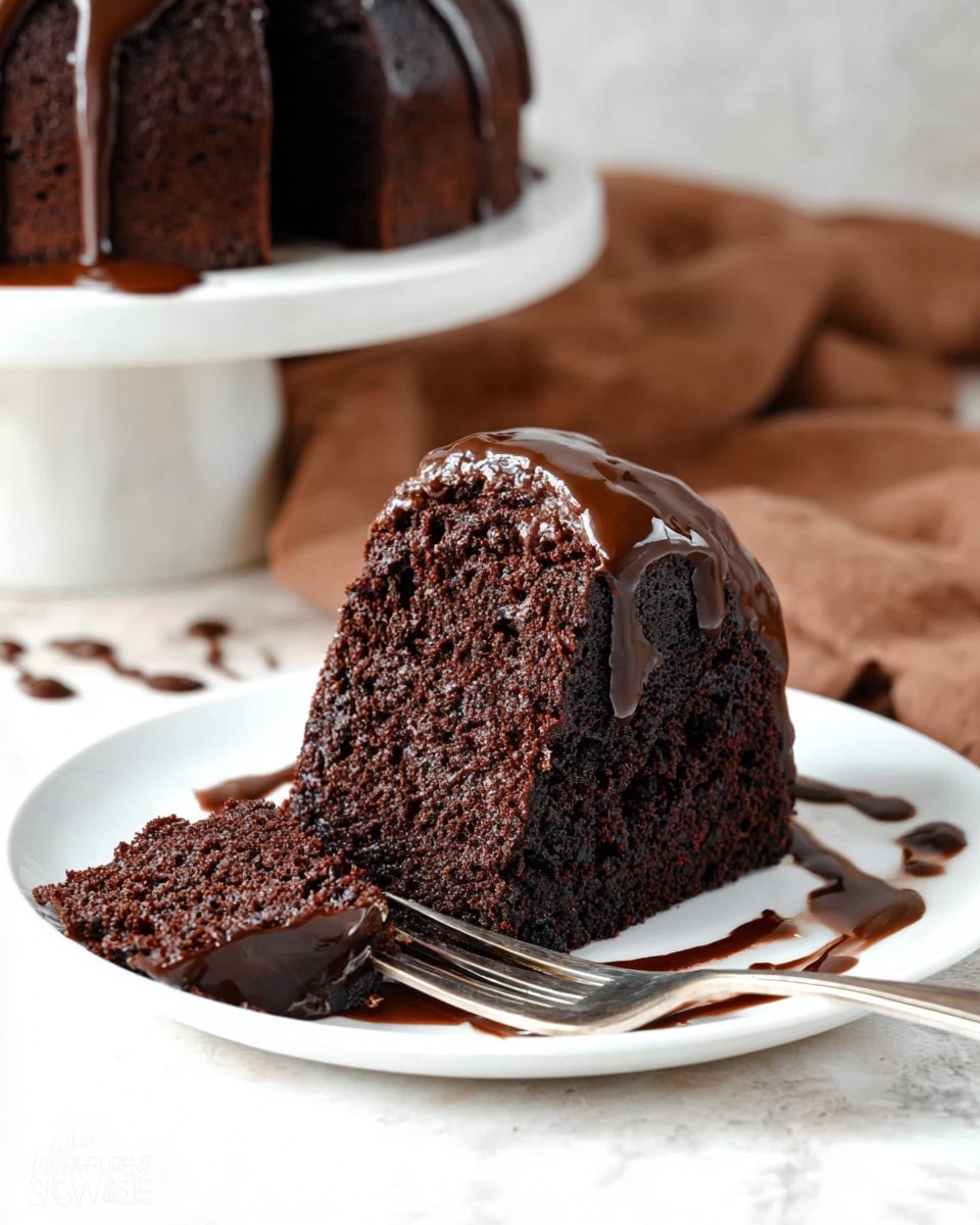 A single thick slice of dark chocolate cake sits on a white plate, topped with a smooth, shiny layer of rich chocolate glaze that drips slightly down the sides. The cake texture looks moist and dense with visible small air pockets. A small piece is cut from the front and rests next to the slice, showing the same deep brown color inside. The plate has chocolate sauce drizzles around the cake, and a silver fork holds the small piece. The background shows a soft brown cloth and another cake on a white stand, all set on a white marbled surface. photo taken with an iphone --ar 4:5 --v 7