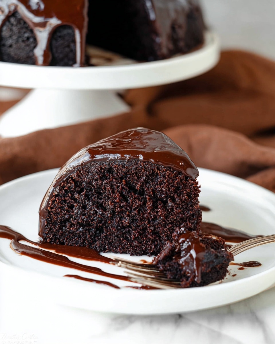 A thick slice of dark chocolate cake sits on a white plate with rich, glossy chocolate ganache smoothly covering the top and slightly dripping down the sides. The cake is dense and moist with a crumbly texture visible where a piece has been cut and rests next to the slice on the plate. A silver fork lies beside the cake with some chocolate sauce drizzled decoratively on the white plate. The background is a white marbled surface with a soft brown cloth blurred in the distance, enhancing the cake’s deep chocolate color. photo taken with an iphone --ar 4:5 --v 7