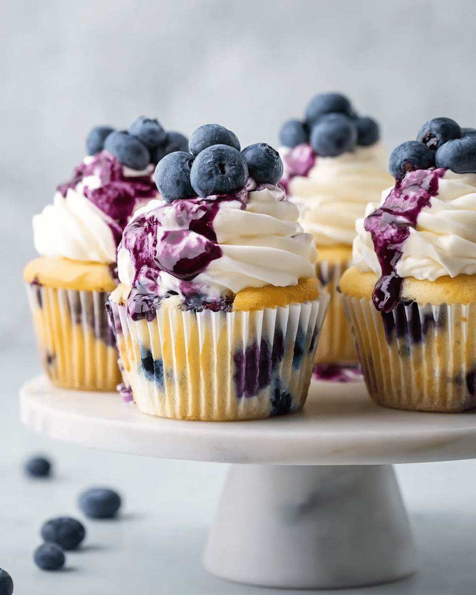 The image shows four blueberry cupcakes arranged on a white marble cake stand. Each cupcake has three main layers: a light yellow cake base with visible blueberries inside, a thick swirl of white cream frosting on top, and a drizzle of rich purple blueberry sauce flowing over the frosting and sides. Fresh whole blueberries are placed on top of the frosting in small clusters. The background is a soft white marbled texture, giving a clean and bright feel to the scene. Photo taken with an iphone --ar 4:5 --v 7