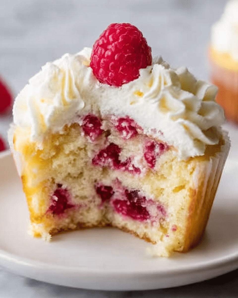 A close-up of a cupcake sliced in half, showing three visible layers inside: the bottom layer is light yellow cake with visible red berry pieces, the middle layer is a dense white cream with more berries mixed in, and the top layer is smooth white cream with a cluster of small red berries. The cupcake is topped with fluffy white whipped cream and a single whole red raspberry on top. The cupcake sits on a simple white plate on a white marbled surface. Photo taken with an iphone --ar 4:5 --v 7