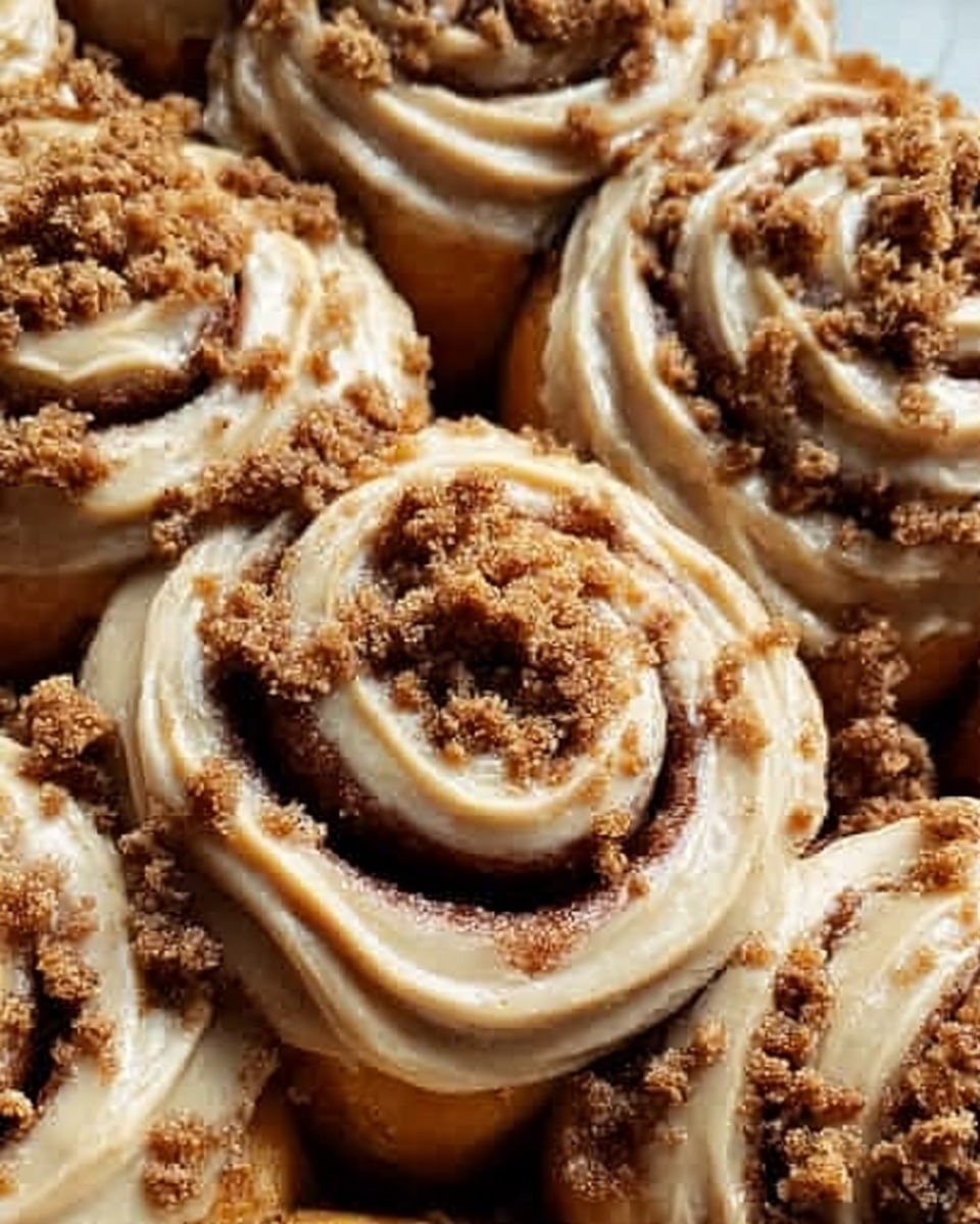 The image shows a close-up of soft, golden brown cinnamon rolls with multiple layers of dough spirals. Each roll is topped with smooth, light brown caramel glaze that is spread evenly and drips slightly down the sides. Crumbled brown sugar pieces are sprinkled generously on top of the glaze, adding a rough, crunchy texture. The cinnamon rolls sit closely together on a white marbled surface that contrasts their warm tones. The lighting highlights the shiny glaze and fluffy dough, making the rolls look fresh and tempting. Photo taken with an iphone --ar 4:5 --v 7